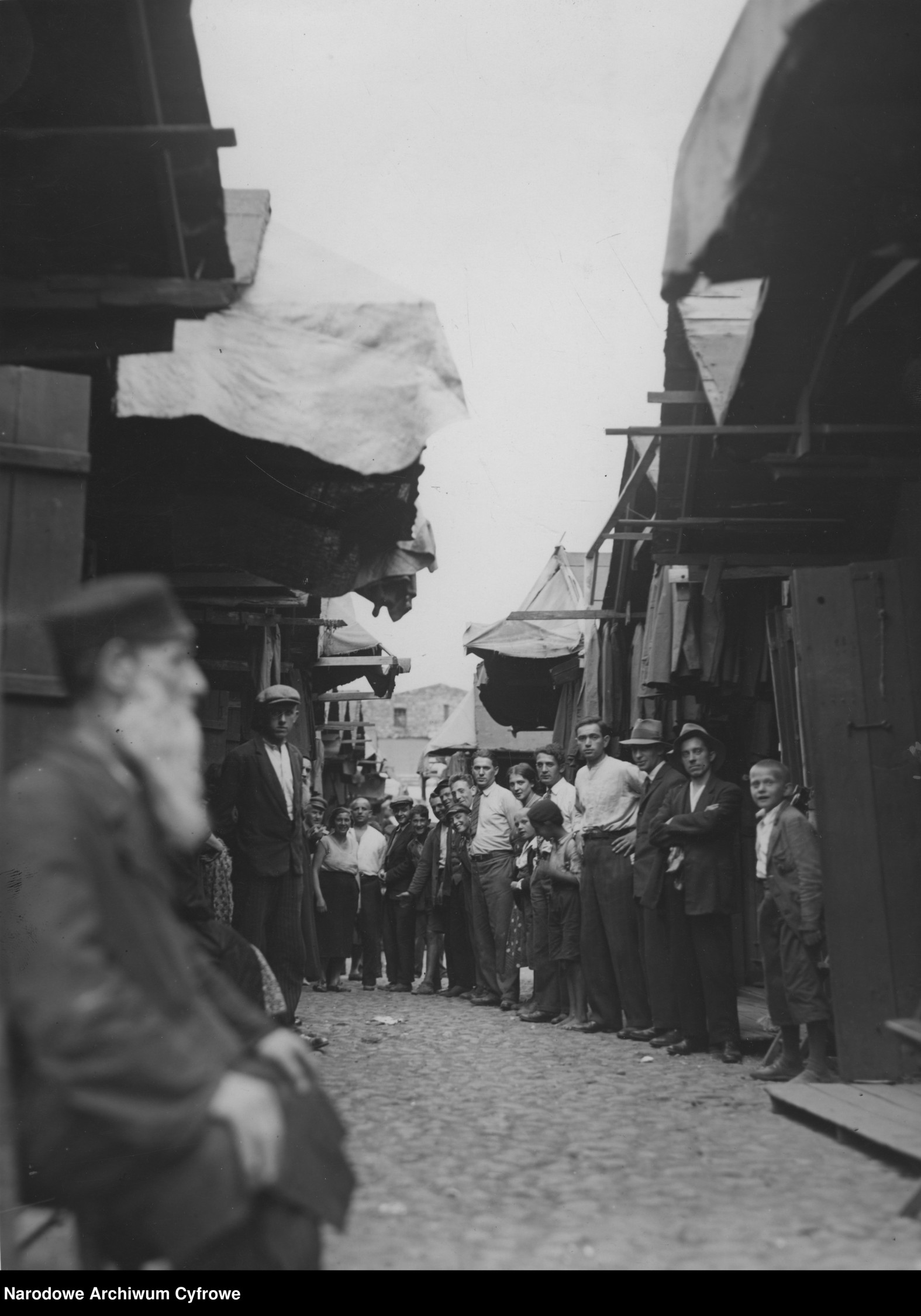 Stragany na targu Kercelak - widok w stronę ul. Ogrodowej. Na pierwszym planie stary Żyd, w tle grupa osób pozujących z dziećmi. Zdjęcie datowane na lata 1926-1935
